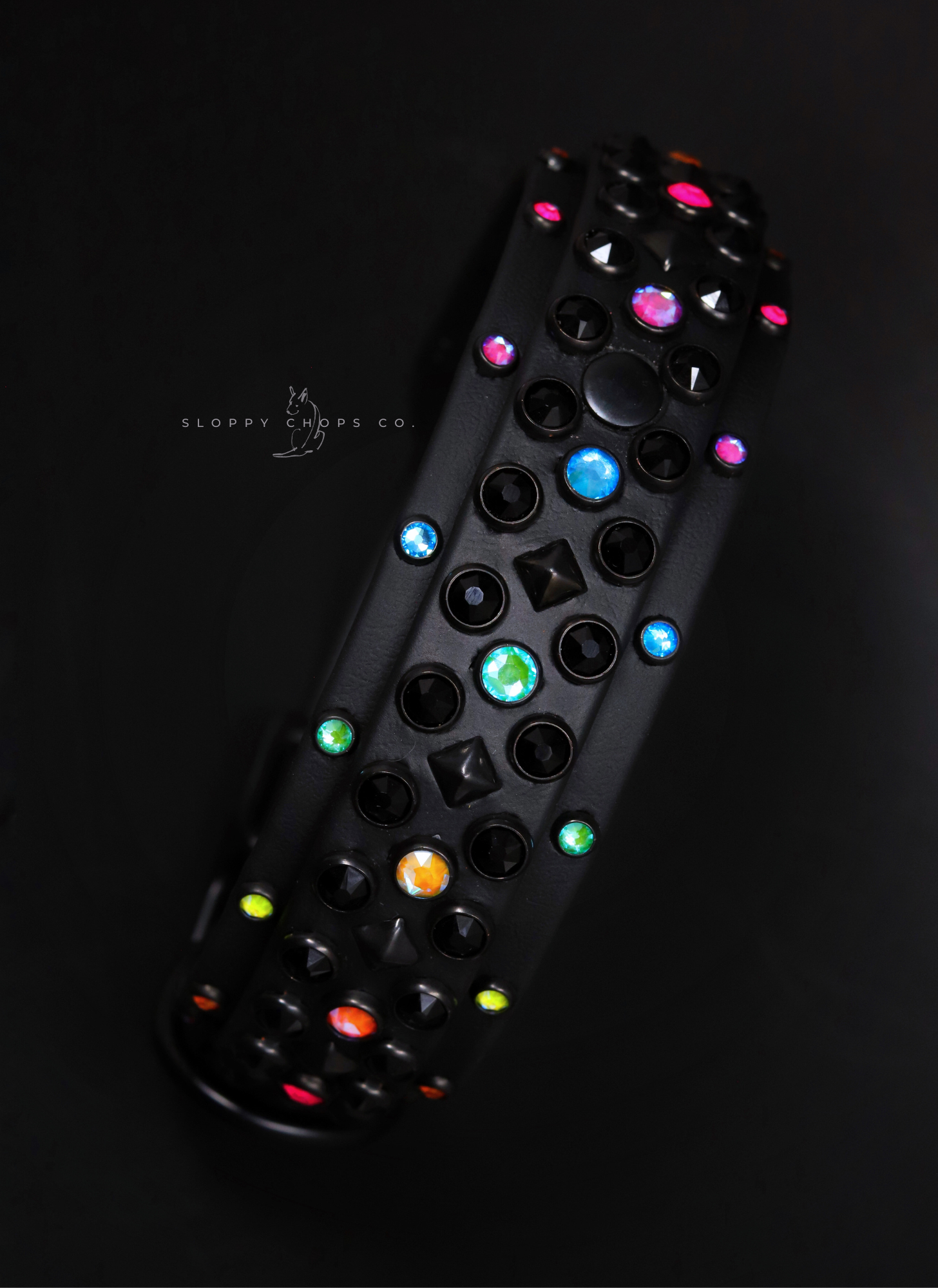 Black leather collar decorated with multicolored gems and matte black studs on dark background